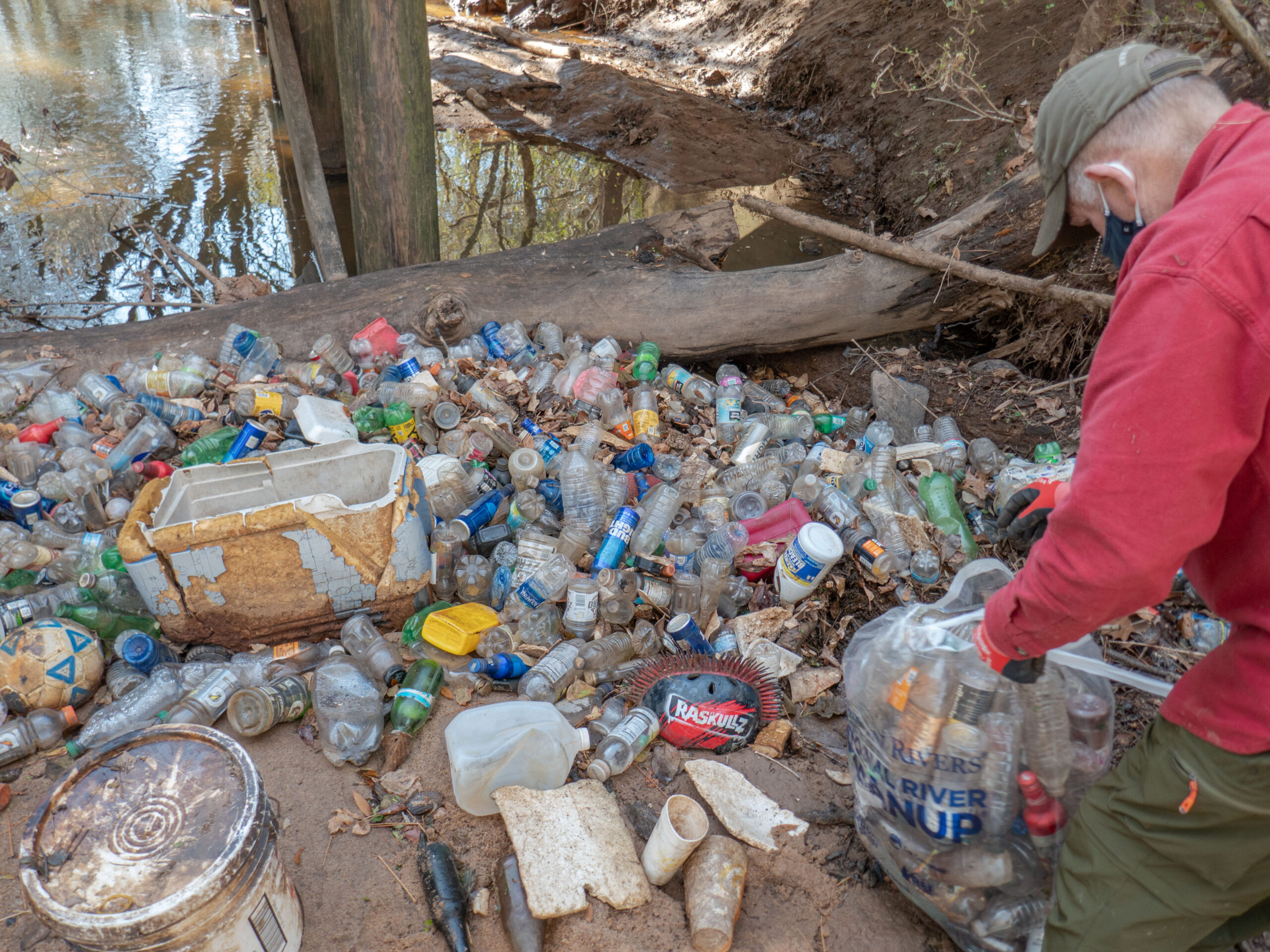 Volunteer picks up trash from a garbage patch outdoors.