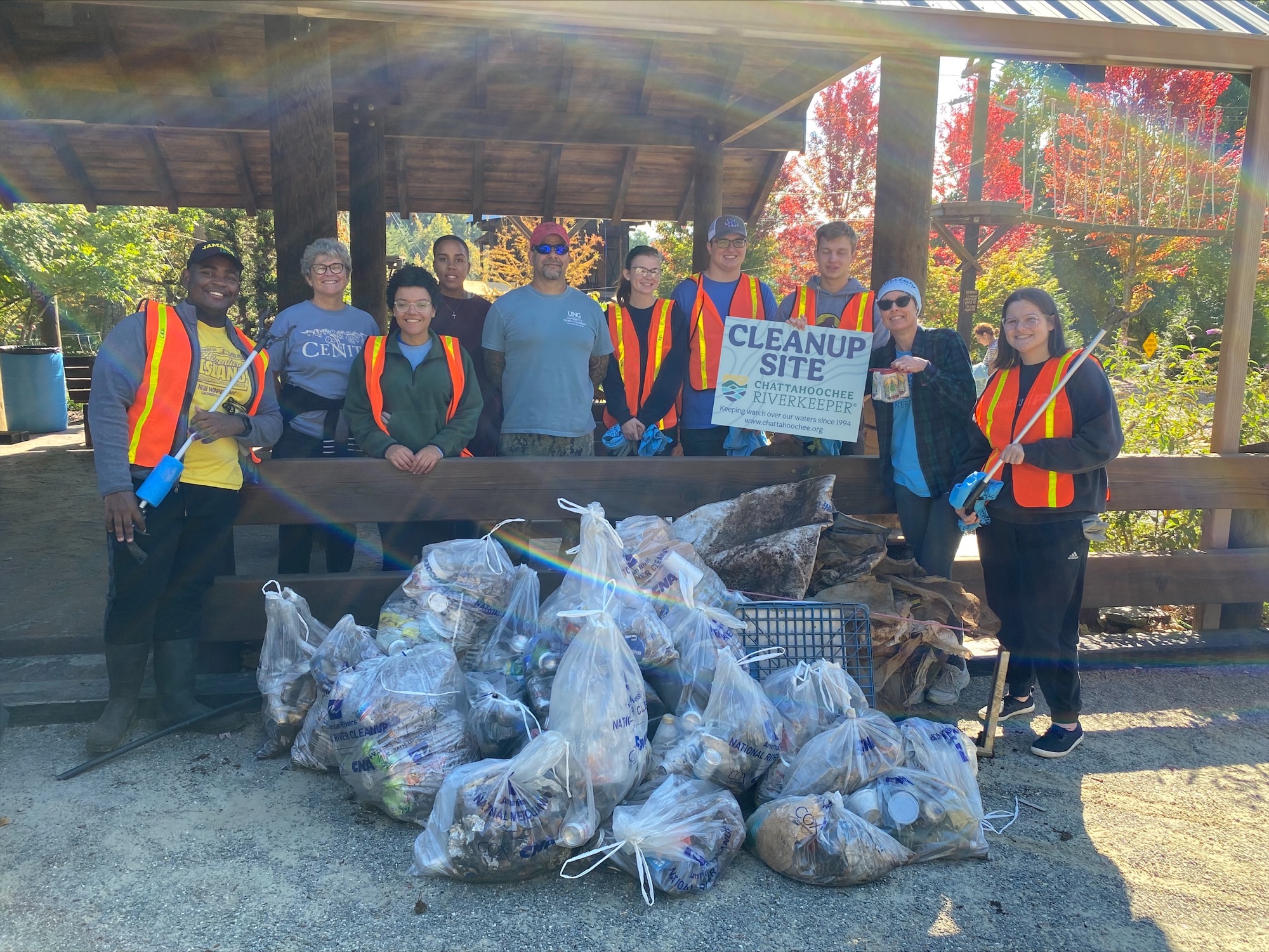 Group of volunteers stands outside with bags of collected trash.