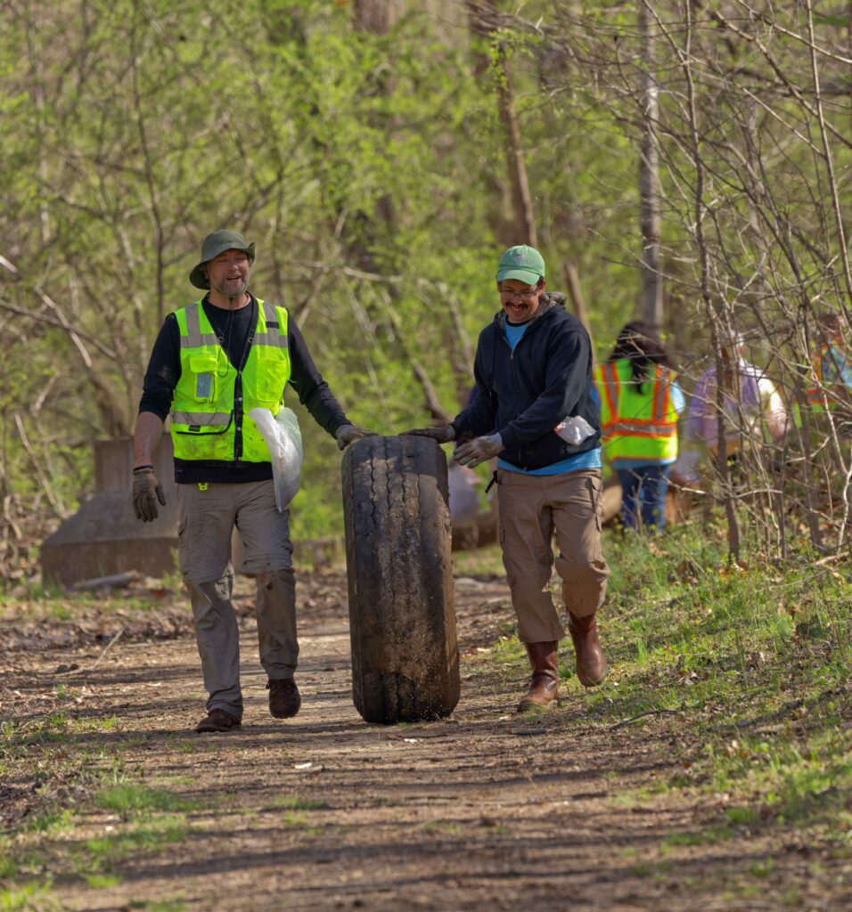 Two volunteers push a large tire up a pathway.