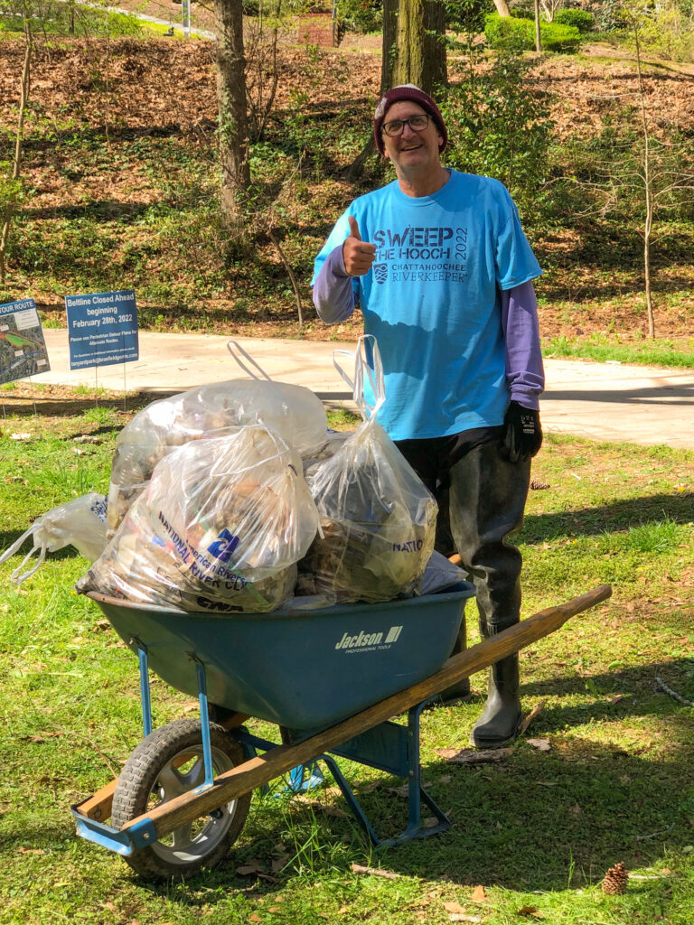 Volunteer gives a thumbs up while posing with a wheelbarrow filled with trash bags.