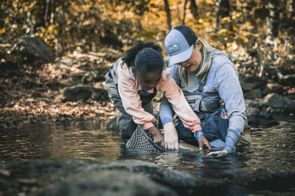 An experienced angler helps a child net a fish at an AKF event.